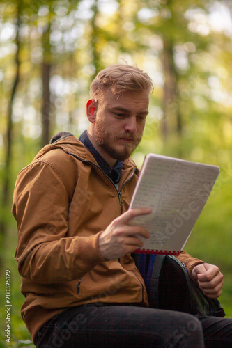 One man reading notebook papers, in forest.