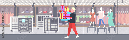 man carrying stack of wrapped gift boxes big seasonal sale shopping concept guy holding colorful presents modern boutique fashion shop exterior flat full length horizontal