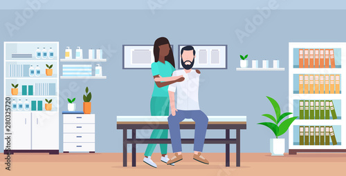 man patient sitting on massage table african american masseuse doing healing treatment massaging patient body manual sport physical therapy concept modern clinic hospital room interior horizontal