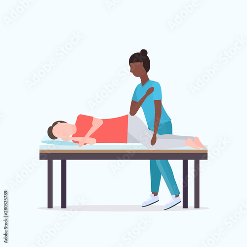 guy lying on massage bed african american masseuse therapist doing healing treatment massaging injured patient manual sport physical therapy rehabilitation concept full length
