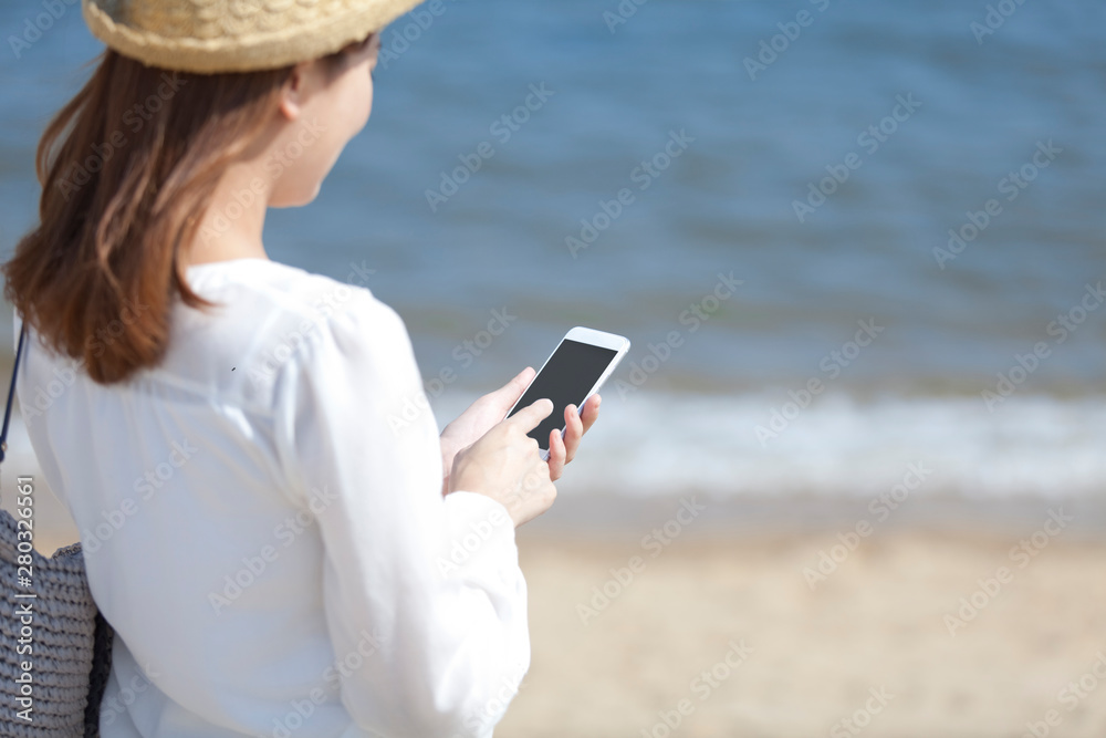 海辺でスマートフォンを操作する女性
