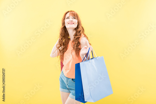smiling redhead girl holding shopping bag isolated on yellow