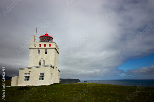 The lighthouse of Dyrholaey stands lonely above the cliffs and trolls fingers at the south coast of Iceland not far from the village of Vik. Cloudy dramatic sky
