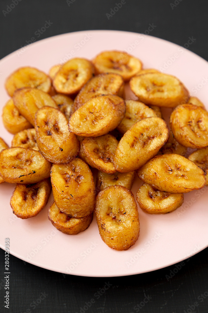 Homemade fried plantains on a pink plate on a black background,  low angle view. Close-up.