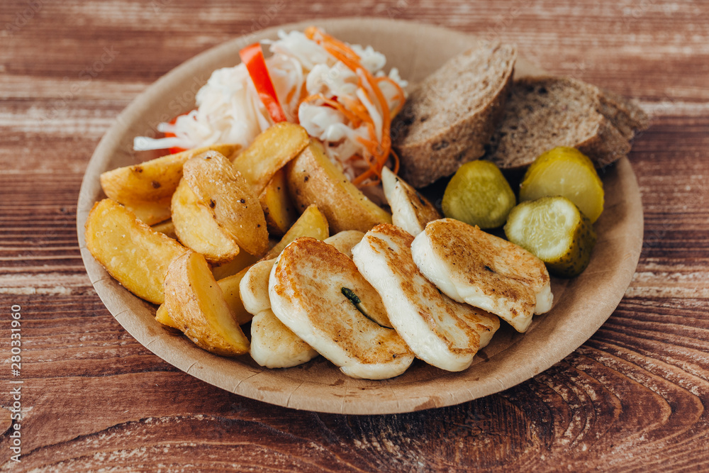 Tasty grilled fish with fried potatoes, cucumber, cabbage and woods in a paper plate on a wooden table. takeaway street food Tasty grilled fish with fried potatoes, cucumber, cabbage and woods in a paper plate on a wooden table. takeaway street food