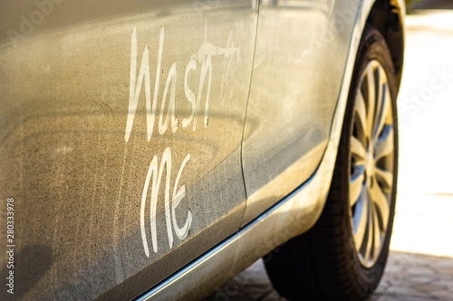 Write the words "wash me" on the very dirty surface of the car. Concept car wash. © Patcharin