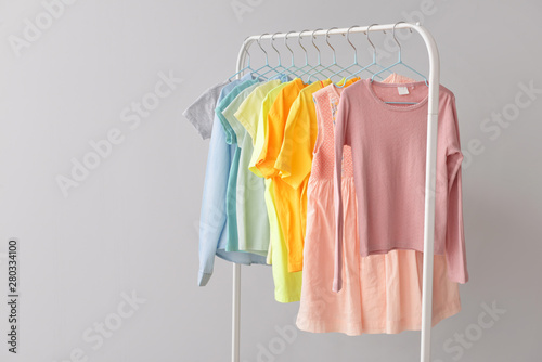 Stylish kid clothes hanging on rack against light background