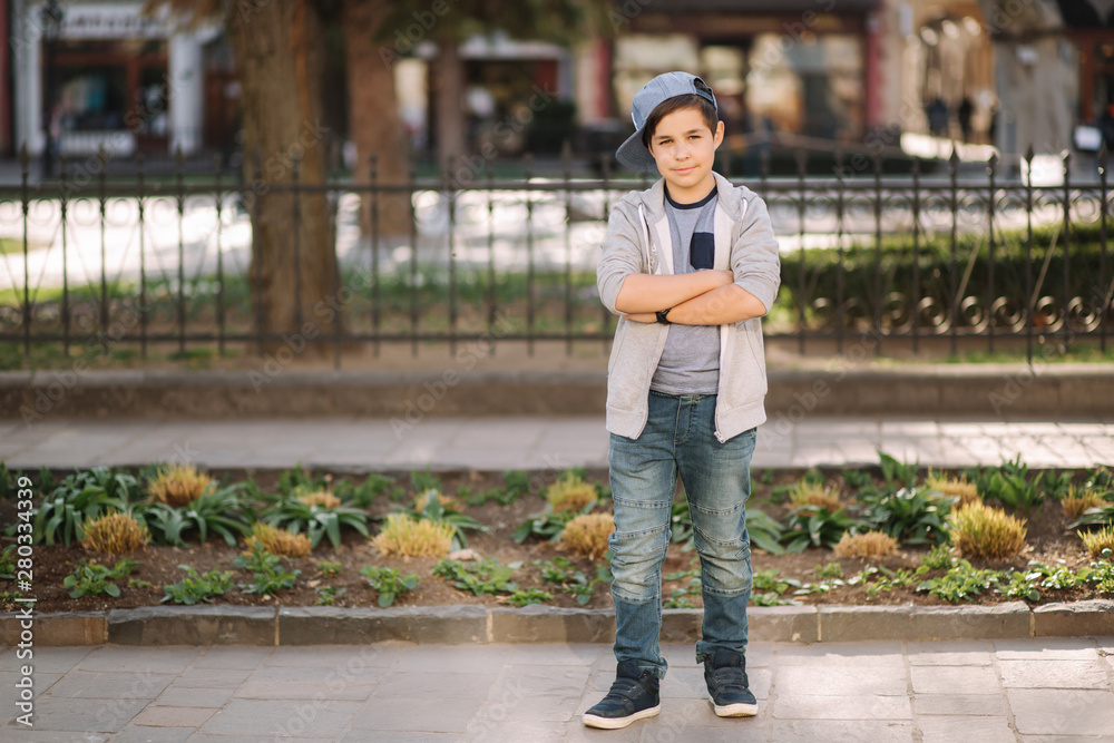 Stylish little school boy in blue cap posing outside for photo. Boy walking in the city in sping summer weather