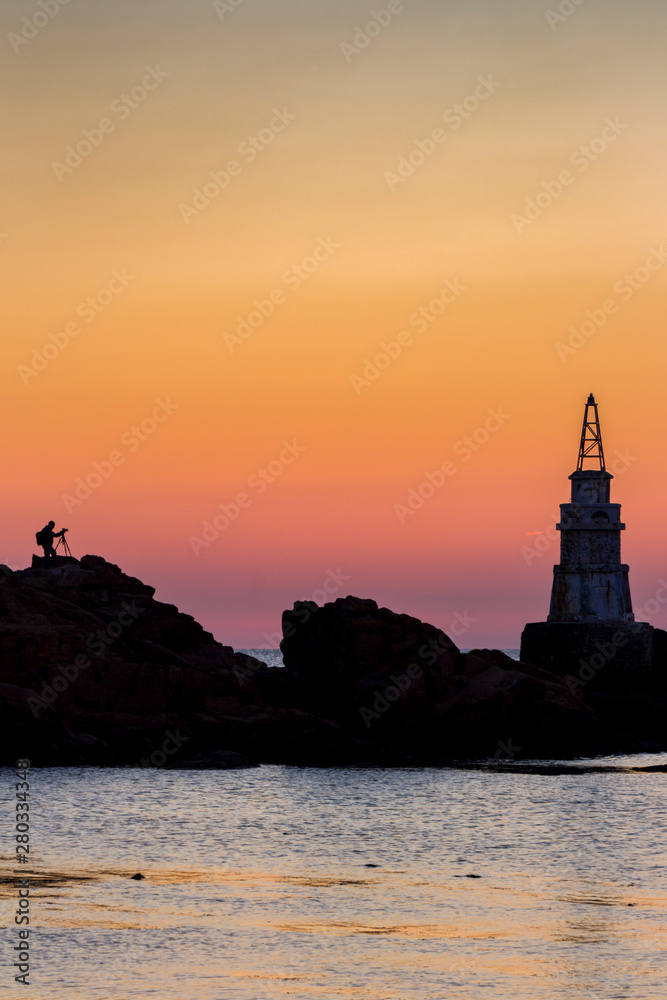 Distant silhouette of a photographer photographing the Ahtopol lighthouse at sunrise, in Ahtopol, Bulgarian Black Sea Coast