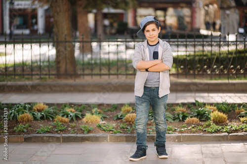 Stylish little school boy in blue cap posing outside for photo. Boy walking in the city in sping summer weather