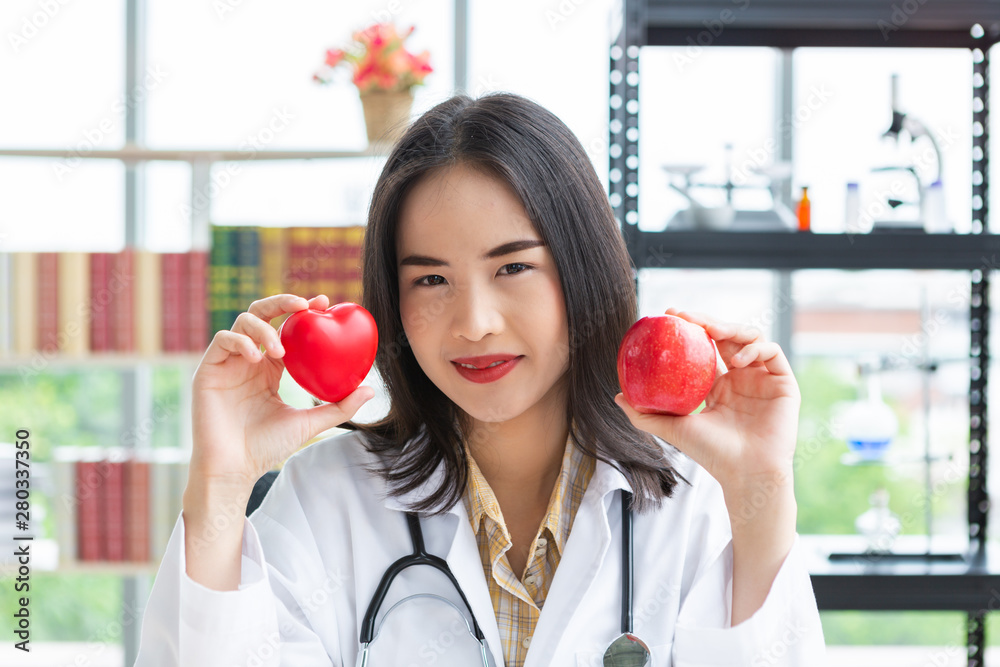 Asian nutritionist doctor woman showing red heart and apple in hand on laboratory room background Asian nutritionist doctor woman showing red heart and apple in hand on laboratory room background