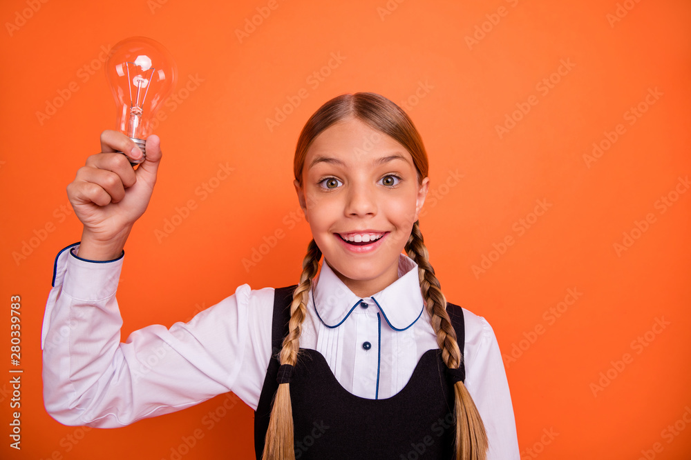 Close-up portrait of her she nice attractive lovely cheerful cheery intellectual nerd pre-teen girl holding in hand bulb new clue isolated over bright vivid shine orange background Close-up portrait of her she nice attractive lovely cheerful cheery intellectual nerd pre-teen girl holding in hand bulb new clue isolated over bright vivid shine orange background