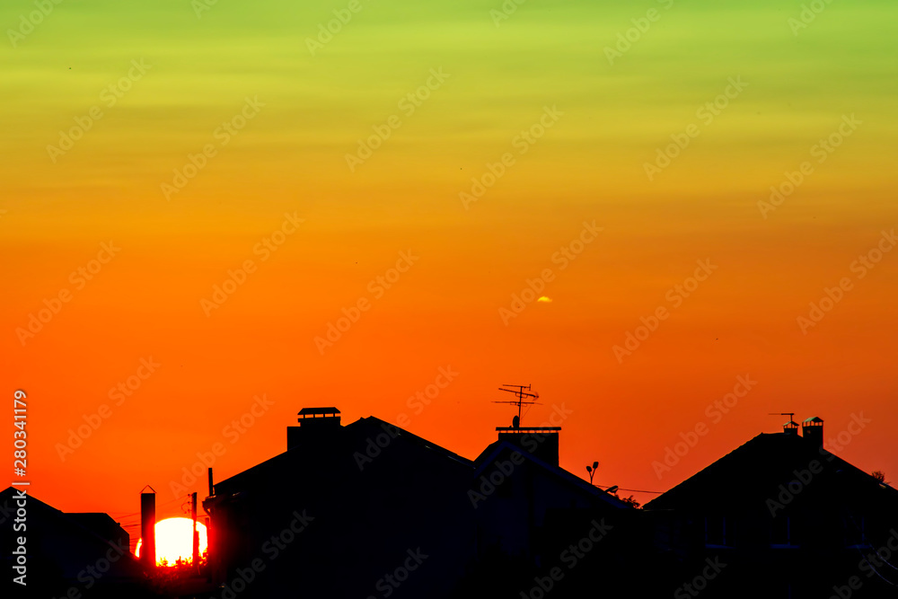 Dark, clear silhouettes of the roofs of houses in the rays of the setting sun. Sunset in the city. Silhouette City landscape in the backlight of the sunset.