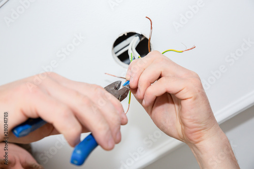 Man is holding pliers in his hands. Electrical insulator for light bulb. Adhesive tape for maintenance repair works in the flat. Restoration indoors. photo