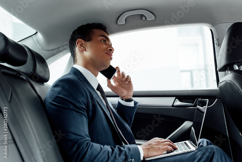 african american businessman in suit using laptop while talking on smartphone in car © LIGHTFIELD STUDIOS