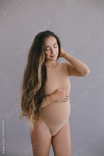 Beautiful pregnant woman with long hair on grey background © polinaloves