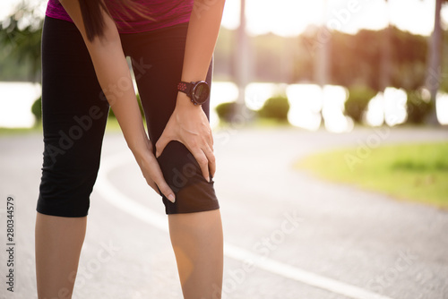 Young fitness woman runner feel pain on her knee in the park. Outdoor exercise activities concept.