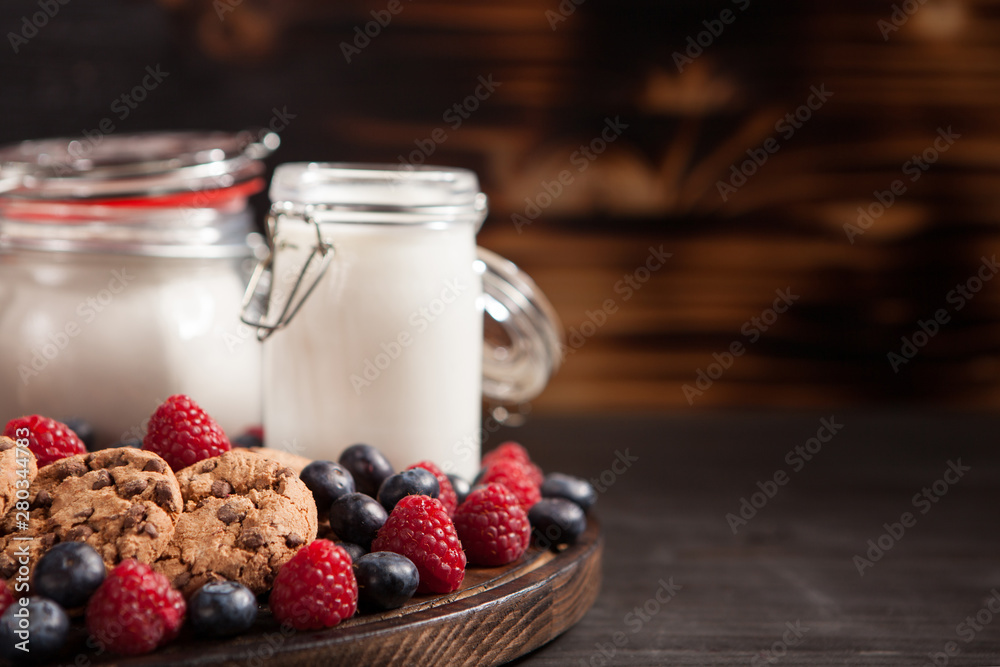 Freshly baked oatmeal chocolate biscuits out of the over with fresh milk on wooden plate Freshly baked oatmeal chocolate biscuits out of the over with fresh milk on wooden plate