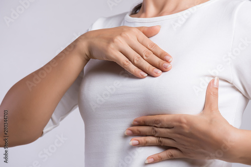 Woman hand checking lumps on her breast for signs of breast cancer on gray background. Healthcare concept.