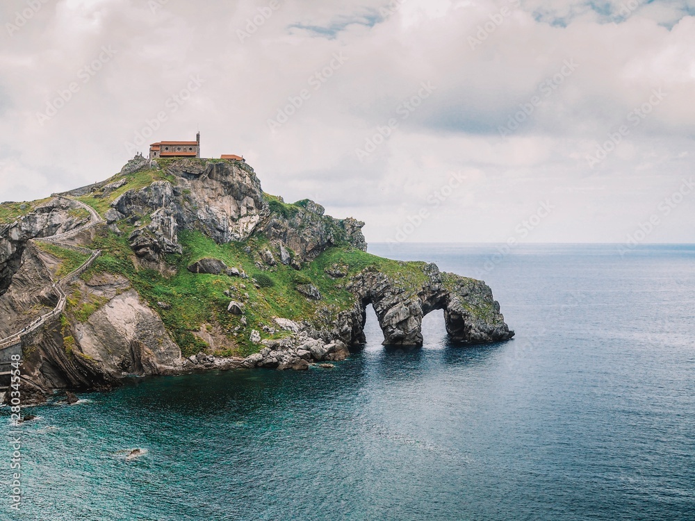 Island Gaztelugatxe on the coast of the Bay of Biscay and looks at the mountain. Spain, Basque Country, winding picturesque picturesque road stairs to the Islands, a lonely island in the ocean