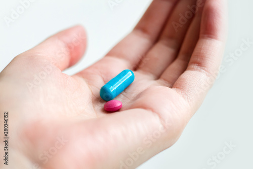 Blue and pink pill capsule on the female palm on white background. Antidepressant pills in female hand. Female hand holding a pill on the palm