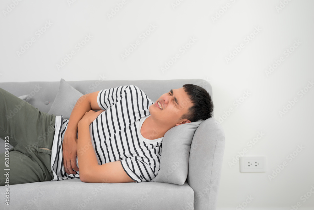 Terrible stomachache. Frustrated handsome young man hugging his belly and keeping eyes closed while lying on the couch at home Terrible stomachache. Frustrated handsome young man hugging his belly and keeping eyes closed while lying on the couch at home