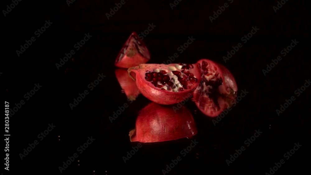 one slice of fresh red pomegranate rotating on a black mirror table. Black background one slice of fresh red pomegranate rotating on a black mirror table. Black background