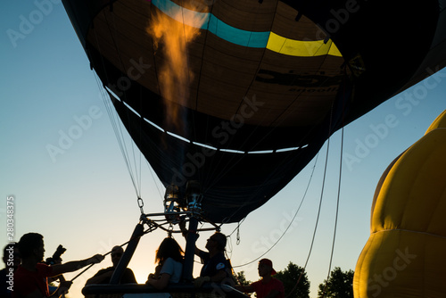 Dark silhouette of sportsman in balloon basket. International meeting of hot air balloons and flying competition. Colourful balloons in the evening skyline. Adventure and freedom, summertime. 