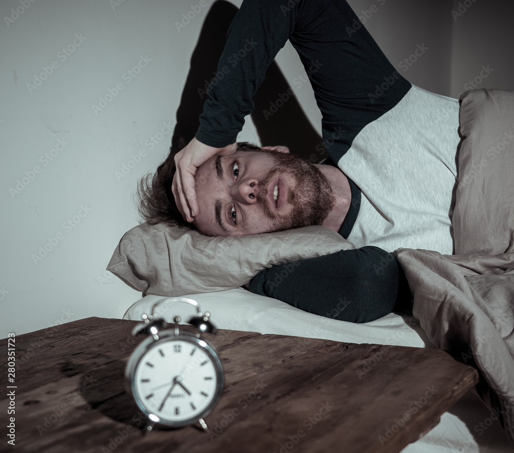 Desperate stressed young man whit insomnia lying in bed staring at alarm  clock trying to sleep Stock Photo | Adobe Stock