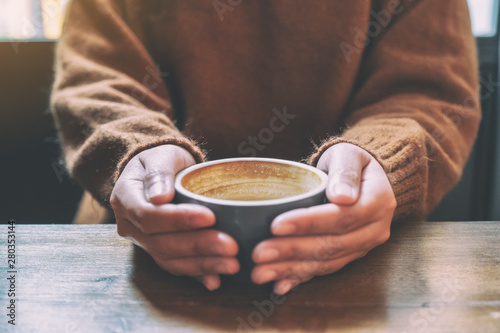 Closeup image of a woman holding a cup of hot coffee on wooden table