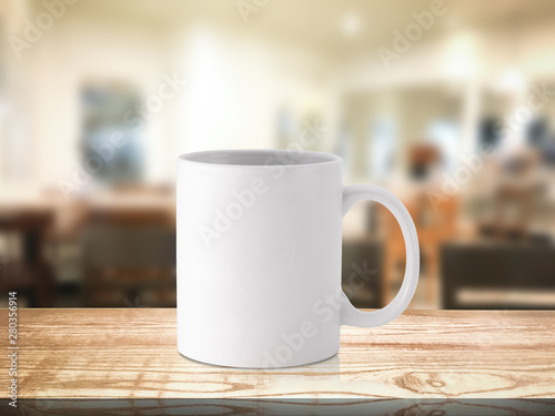 White coffee mug or drink cup on blur restaurant or desserts cafe interior store background. Wooden shelf backdrops with mugs for design.
