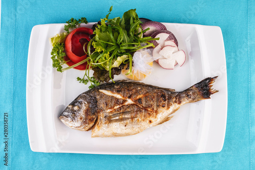Mediterranean dish, European cuisine. whole fish baked in the oven, served with a salad of vegetables, greens, arugula, onion rings, tomato and lemon