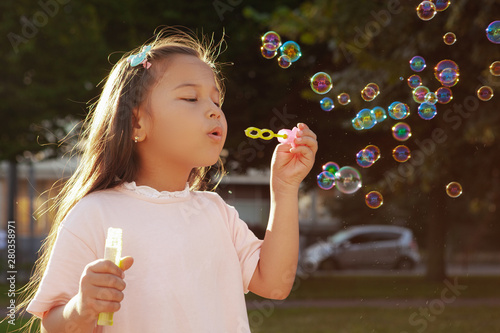 Close up of a lovely little Asian girl blowing bubbles in the park  copy space. Adorable little girl having fun outdoors  blowing bubbles in sunlight