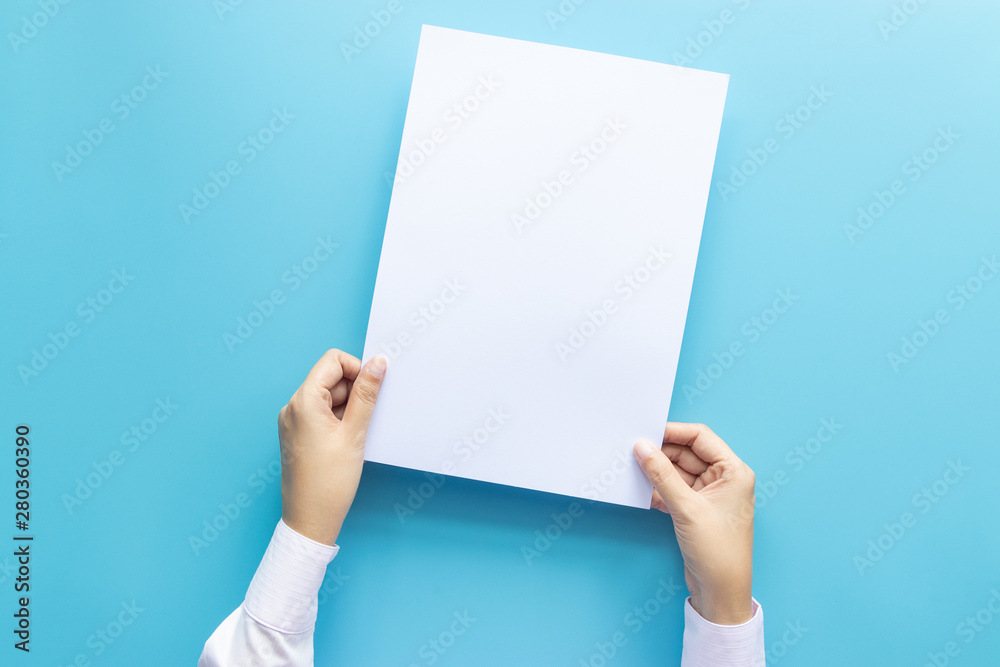 close up hands holding empty white blank letter paper size A4 for flyer or invitation mock up isolated on a blue background. close up hands holding empty white blank letter paper size A4 for flyer or invitation mock up isolated on a blue background.