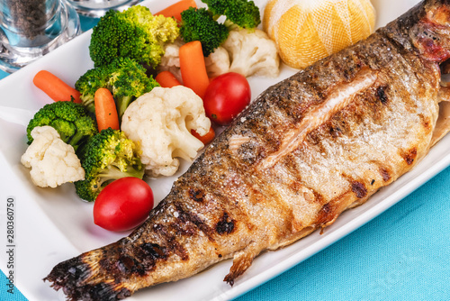Mediterranean dish, European cuisine. whole fish baked in the oven, served with steamed vegetables - cauliflower, broccoli, carrots, cherry tomatoes and lemon