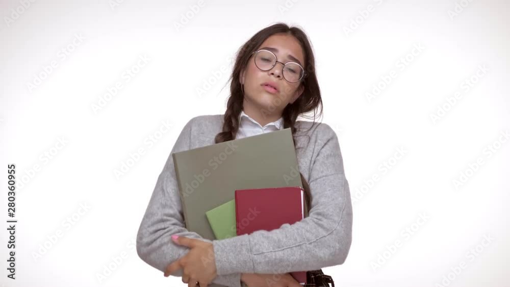 Cute young brunette girl student with books getting tired while looking at the camera over white background isolated Cute young brunette girl student with books getting tired while looking at the camera over white background isolated