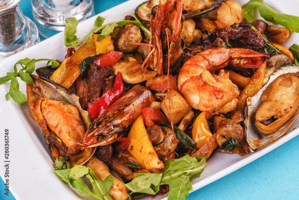 Mediterranean dish, European cuisine. Braised shrimps, mussels, squids with vegetables, red and green pepper, tomatoes, greens, arugula and mushrooms Mediterranean dish, European cuisine. Braised shrimps, mussels, squids with vegetables, red and green pepper, tomatoes, greens, arugula and mushrooms