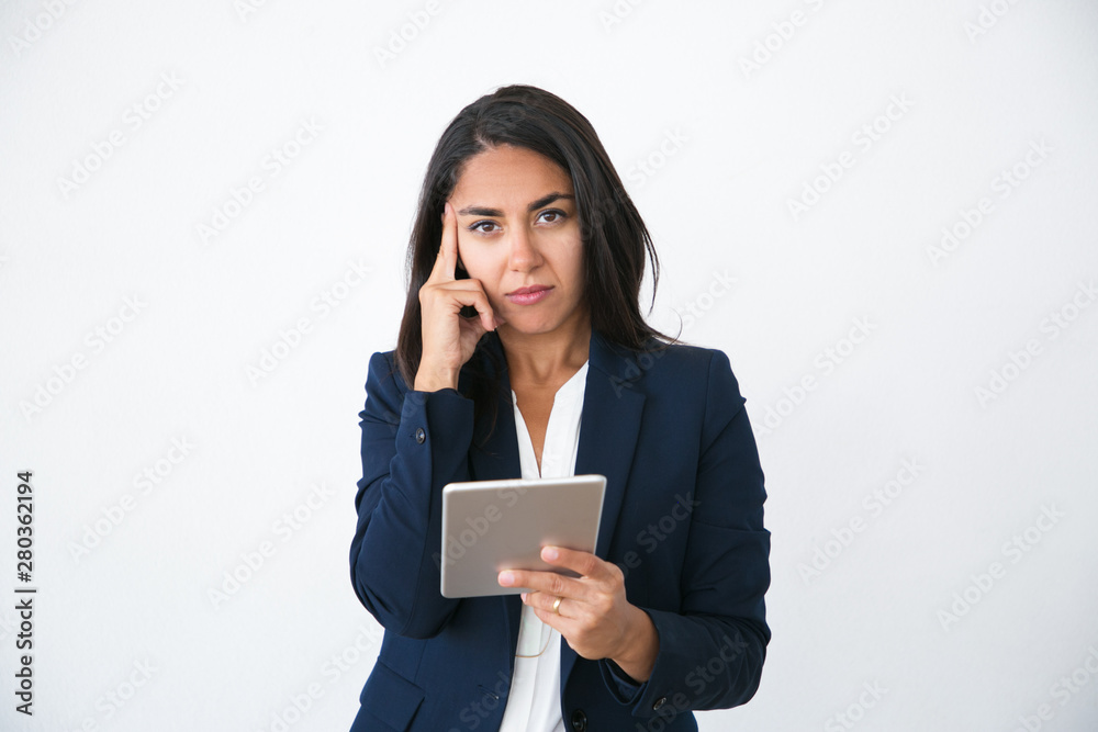 Serious pensive business woman using internet app on tablet. Young Latin woman in office jacket holding digital devise and looking at camera. Online app concept Serious pensive business woman using internet app on tablet. Young Latin woman in office jacket holding digital devise and looking at camera. Online app concept