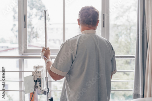 A man stands in a hospital ward and looks out the window. Dropper in a mans hand in a hospital.