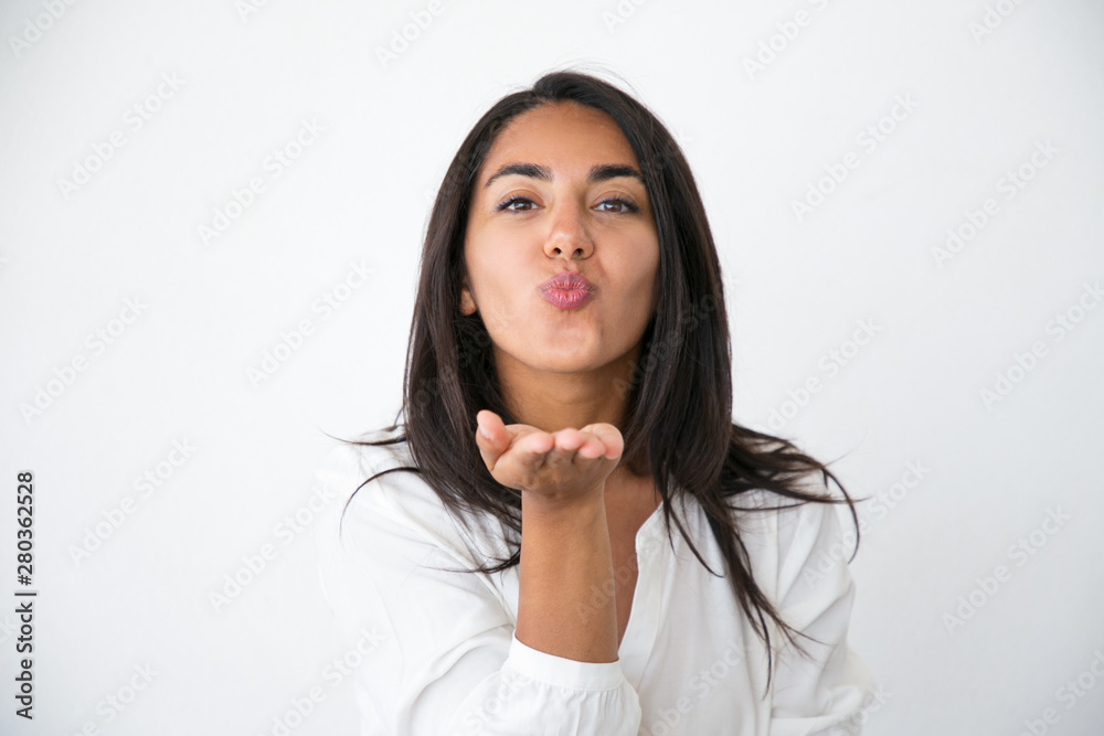 Joyful cute woman sending air kiss at camera. Beautiful young Latin woman in white shirt blowing kiss. Tenderness or love concept