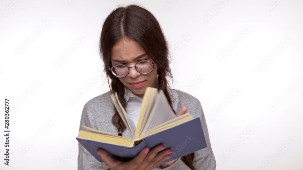 Emotional young brunette girl student nervously looking for some information in the book over white background isolated Emotional young brunette girl student nervously looking for some information in the book over white background isolated