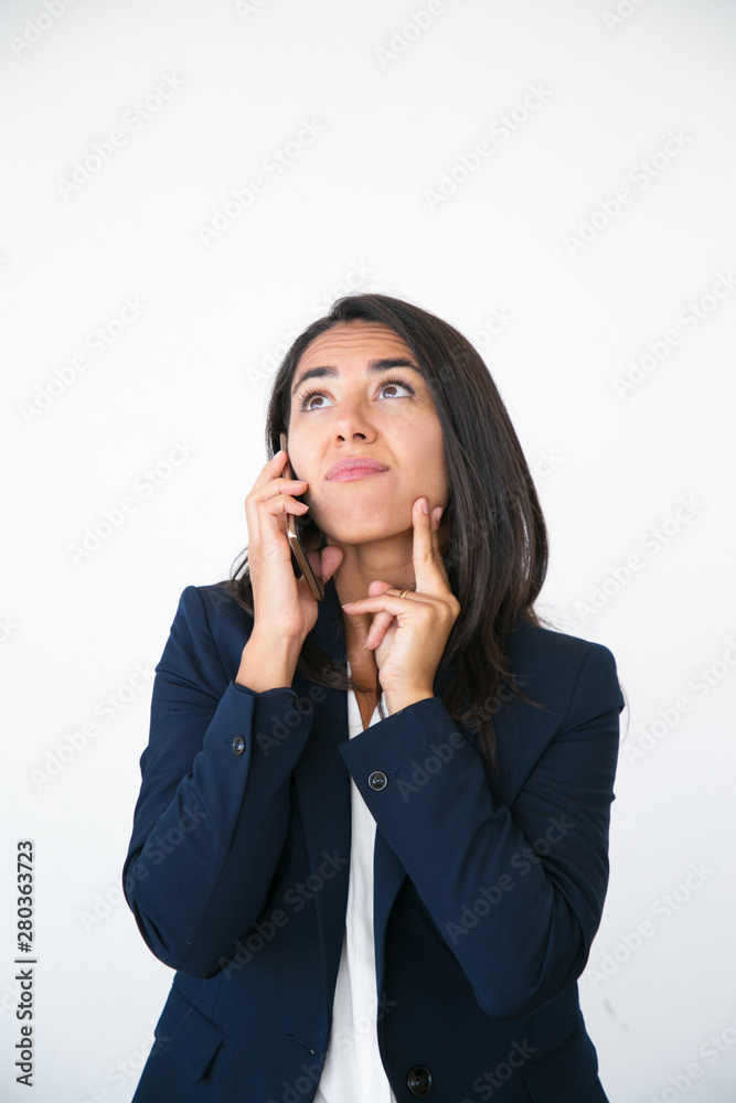 Pensive excited business woman talking on phone and studying information overhead. Young Latin woman speaking on cellphone and looking up. Presenting concept Pensive excited business woman talking on phone and studying information overhead. Young Latin woman speaking on cellphone and looking up. Presenting concept