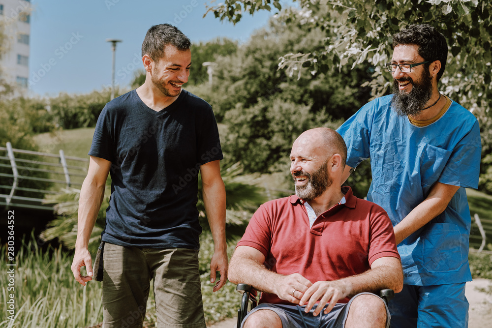 a man on wheelchair with his assistant and a friend - outdoor