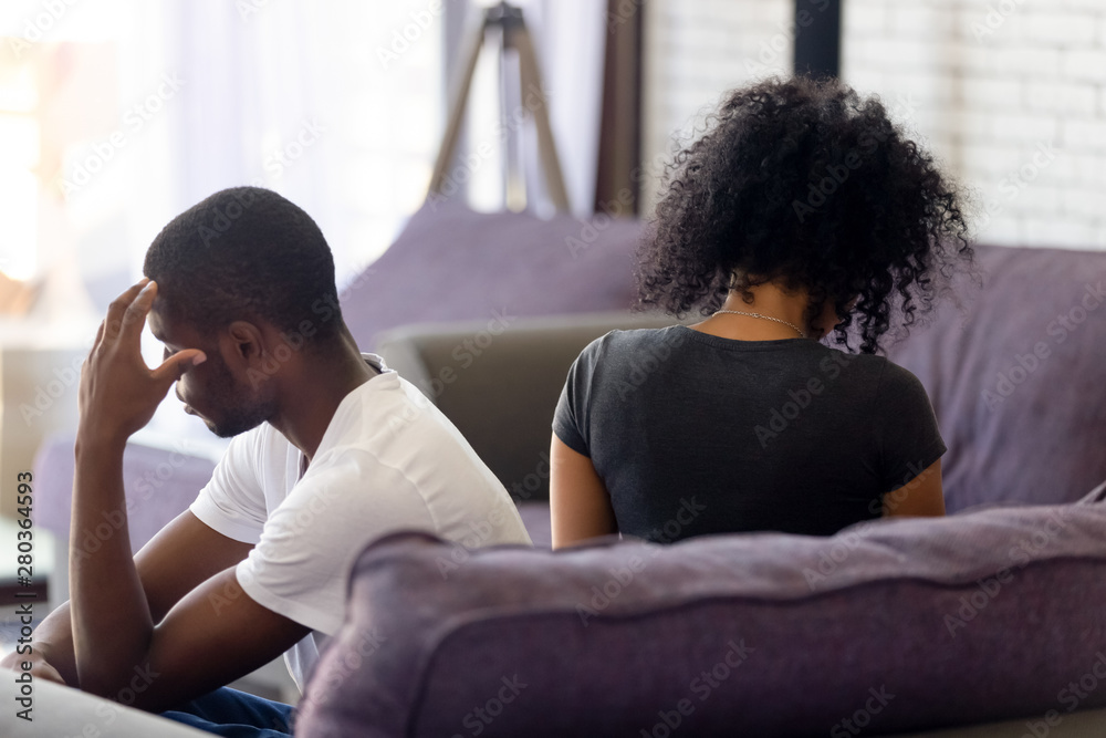 Rear view black couple sitting separately on couch not talking Rear view black couple sitting separately on couch not talking