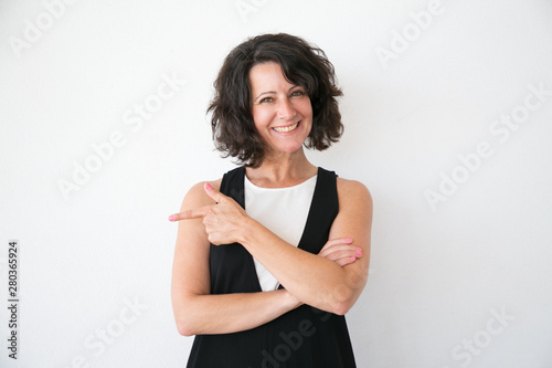 Happy cheerful woman in casual presenting store or product. Middle aged business lady standing over white studio background, pointing finger away and smiling. Advertising concept