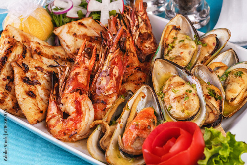 European cuisine, Mediterranean dish. Plate with assorted sea grill. Fried fish, king prawns with lemon, mussels with oyster sauce, colmar rings, crab meat