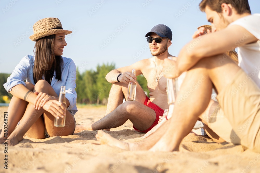 Group of happy young people sitting together at the beach talking and drinking beers