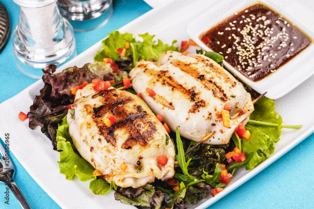 European cuisine, Mediterranean dish. Stuffed squid on a leaf of lettuce with greens, tomatoes, cheese and red onions with oyster sauce European cuisine, Mediterranean dish. Stuffed squid on a leaf of lettuce with greens, tomatoes, cheese and red onions with oyster sauce