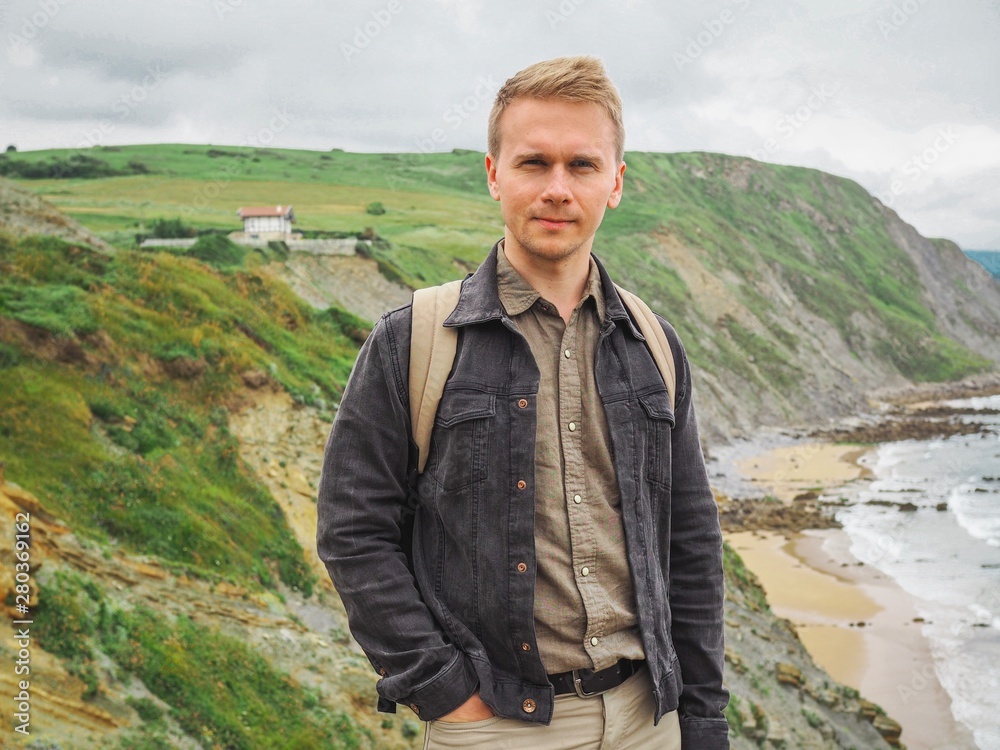 Blond man sitting on a stone overlooking the coastline of the Bay of Biscay, mountain view, beach, stones Blond man sitting on a stone overlooking the coastline of the Bay of Biscay, mountain view, beach, stones