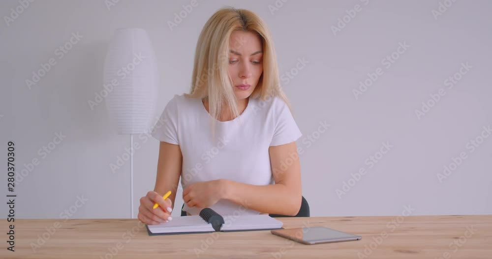 Closeup portrait of adult caucasian blonde businesswoman using the tablet and taking notes indoors in the office at the desk Closeup portrait of adult caucasian blonde businesswoman using the tablet and taking notes indoors in the office at the desk